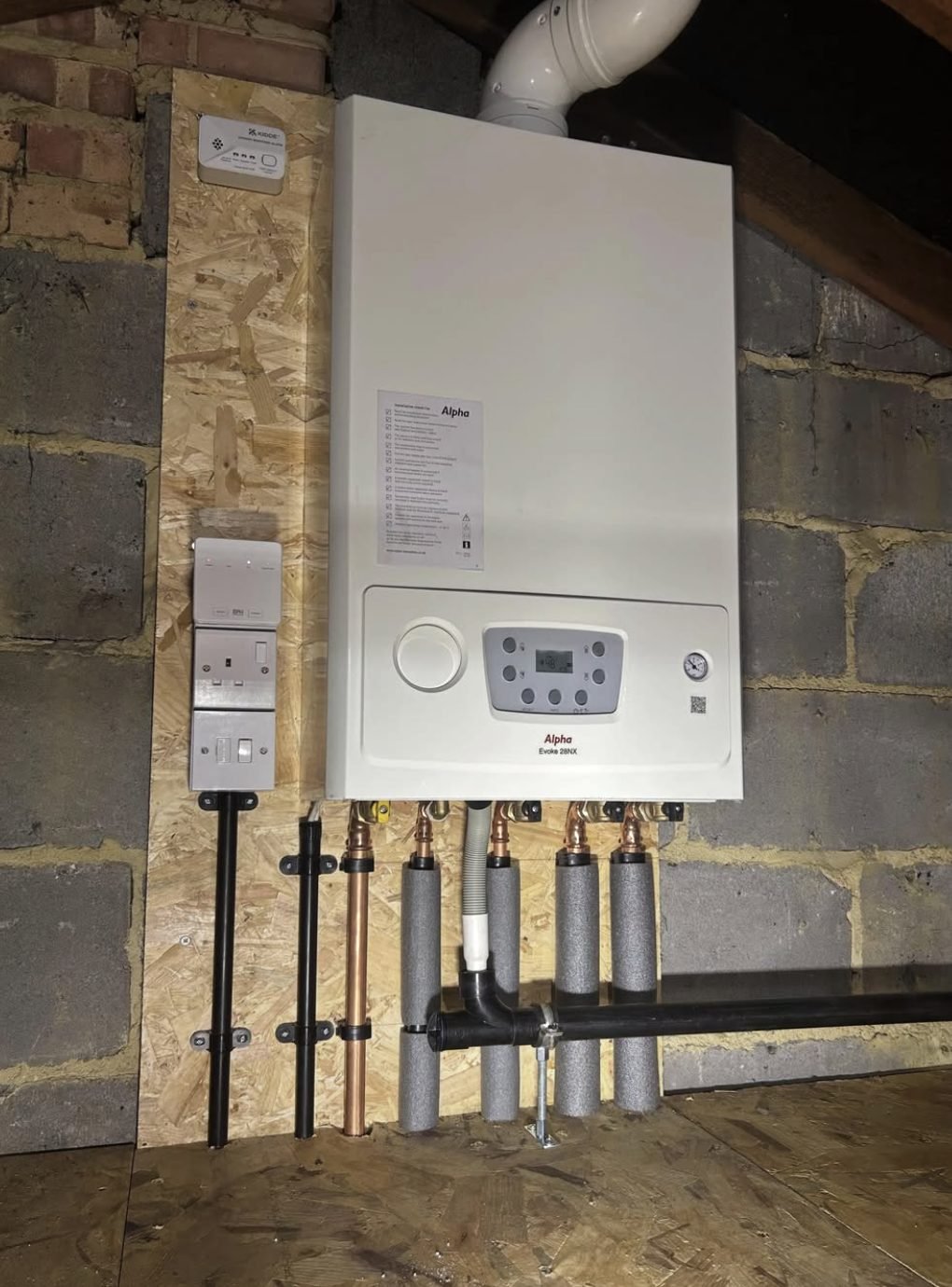 Alpha combi boiler installed in a loft on a ply board with insulated pipework and a CO alarm