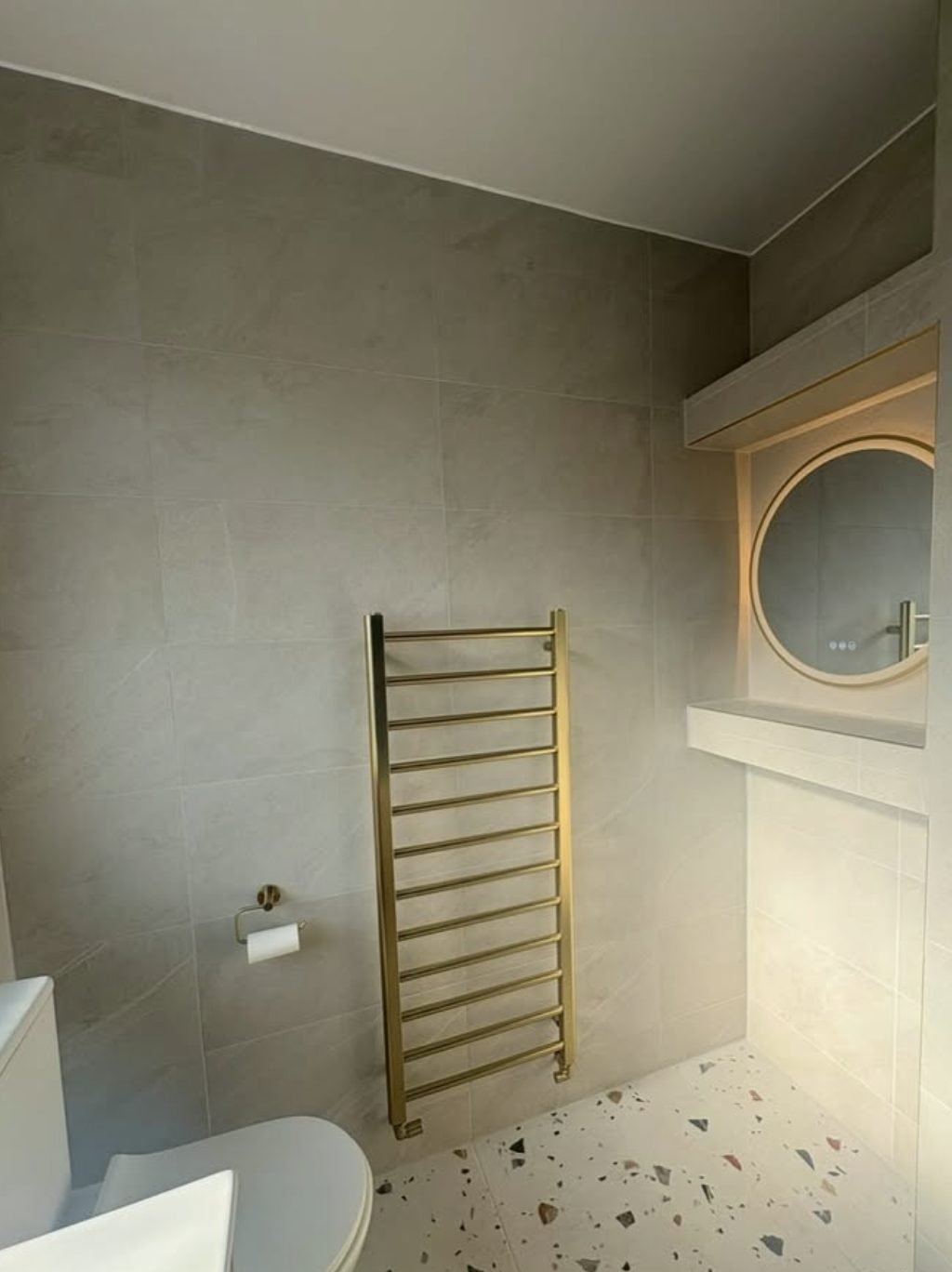 Brushed gold ladder towel rail fitted in a tiled bathroom
